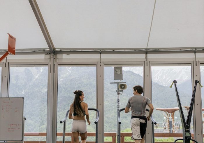 Back view of a couple running on treadmills in a gym with a scenic mountain view.
